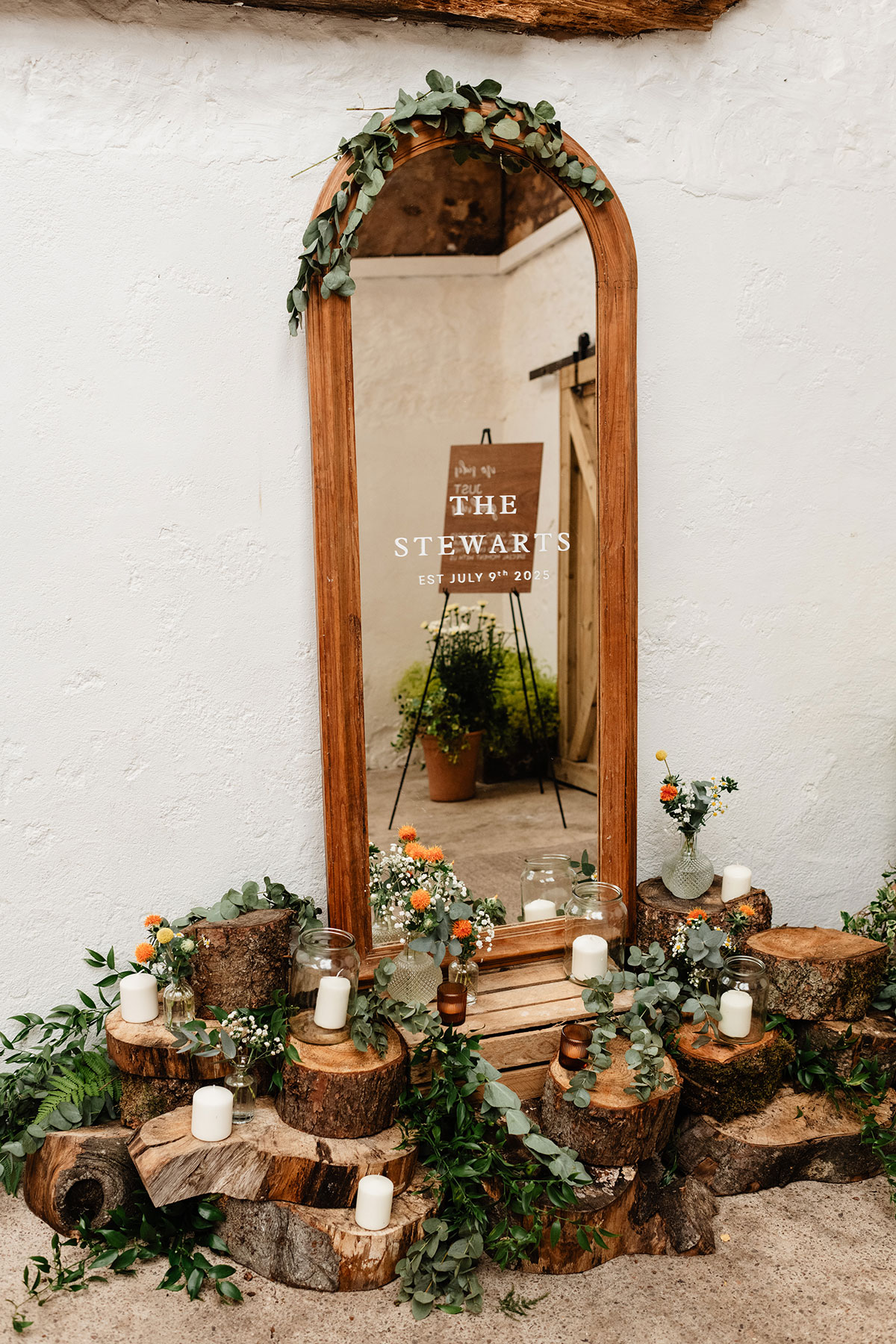 all wooden-framed mirror decorated with eucalyptus and candles, featuring a vinyl welcome sign reading “The Stewarts, Est July 9th 2025”
