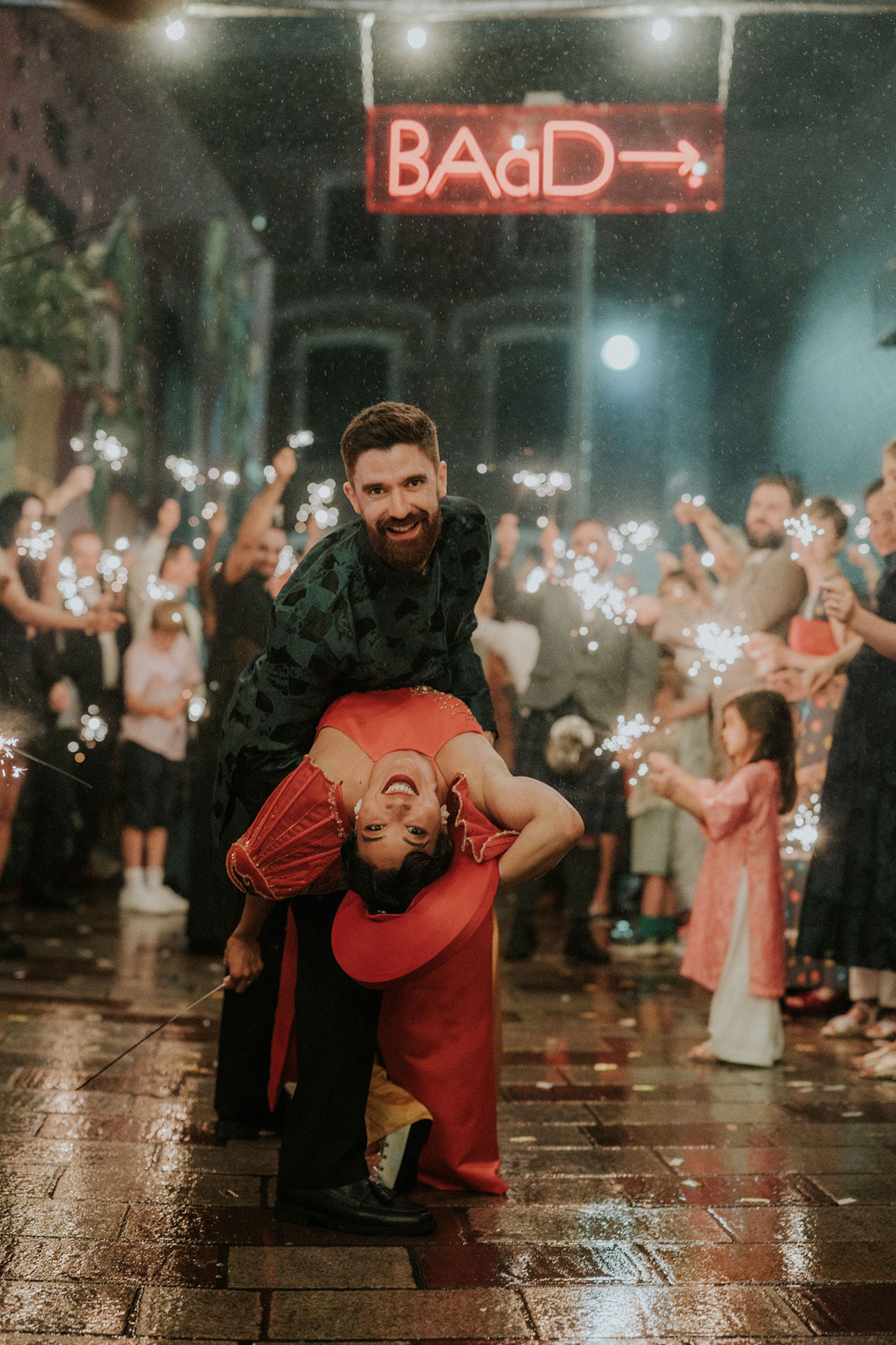 BAaD wedding couple dancing beneath the neon Barras Art and Design sign as guests hold sparklers in Glasgow.