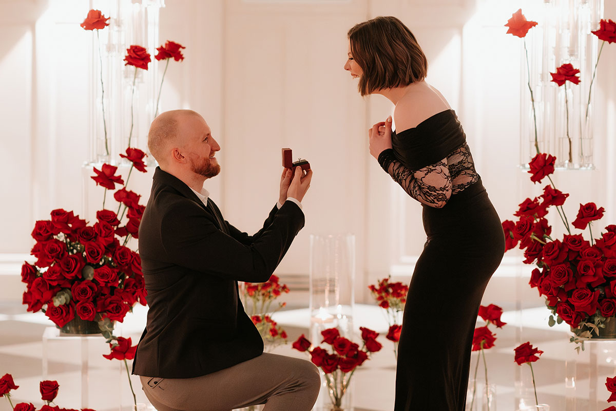 Groom-to-be proposing with an engagement ring surrounded by red rose floral styling