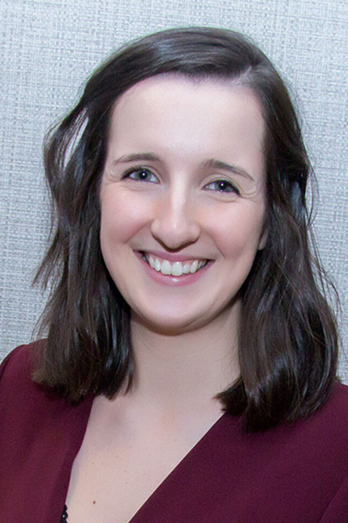Smiling female wedding supplier portrait against neutral background, natural makeup and shoulder-length dark hair