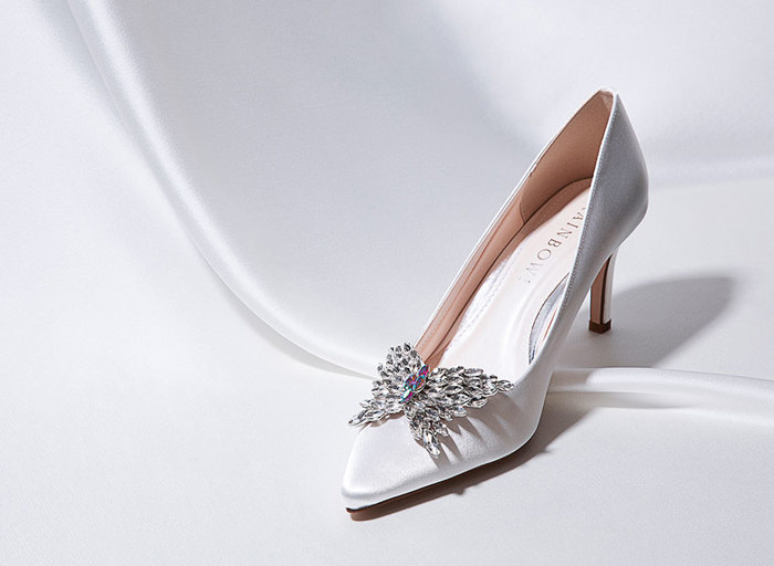 A high heel shoe in white with a bejeweled butterfly clip added on the front 