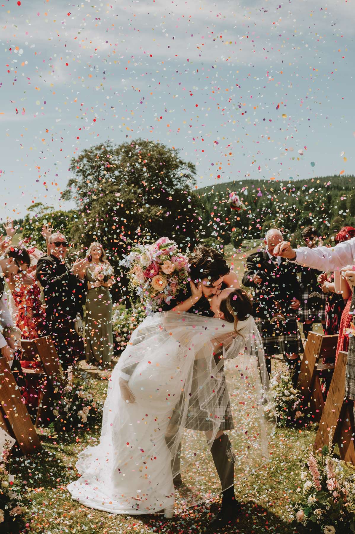 Newlyweds kiss beneath colourful confetti after their outdoor Ballogie House wedding ceremony