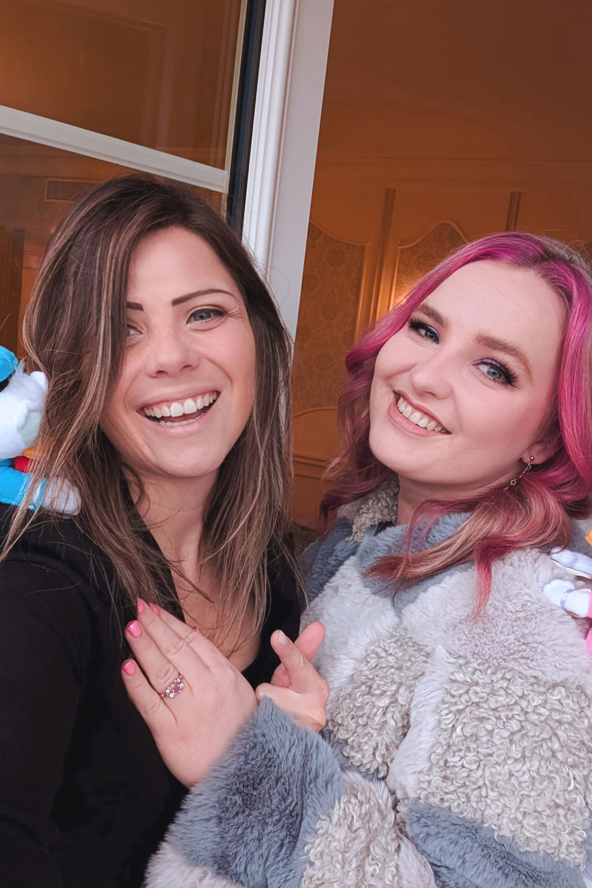 Katie and Mel smiling together as Katie shows her bespoke pink gemstone engagement ring