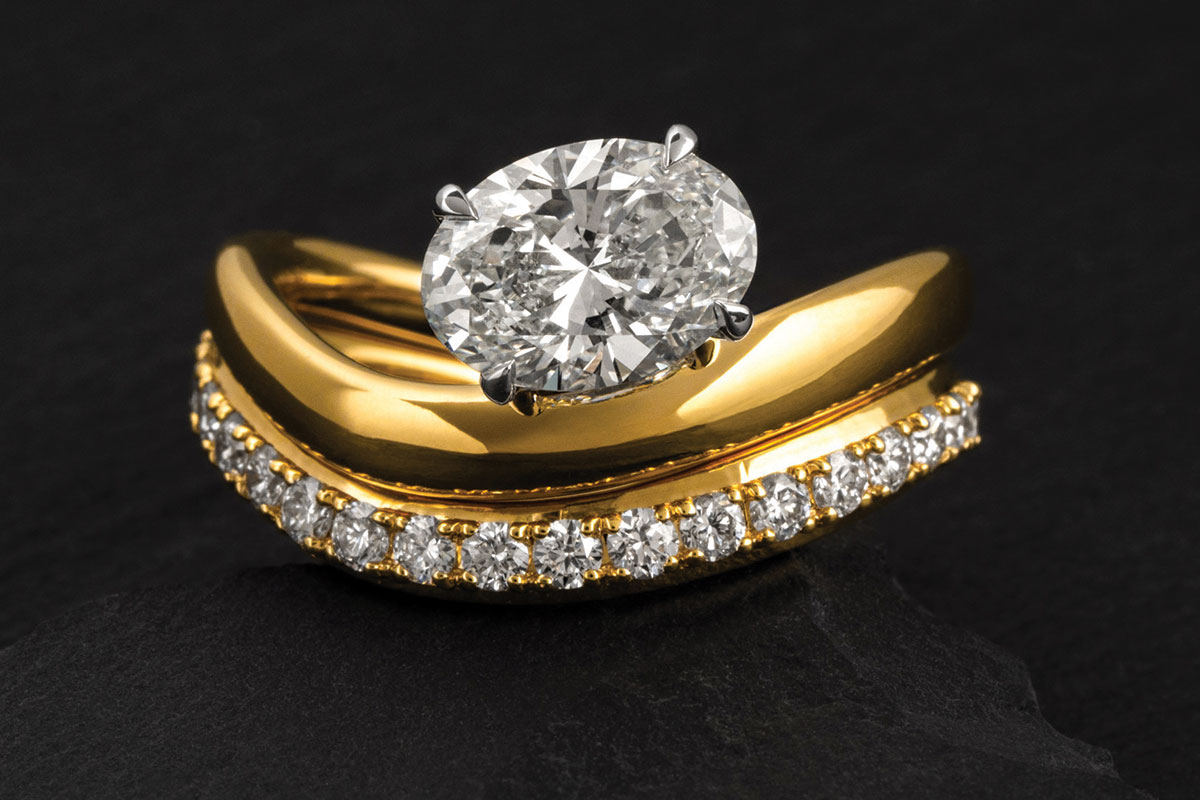 Oval diamond engagement ring paired with curved yellow gold diamond wedding band by James Porter & Son