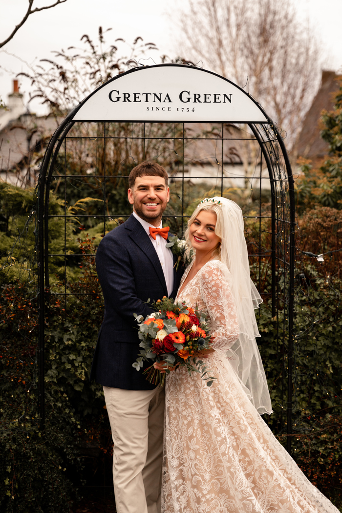 bride and groom smiling under gretna green sign