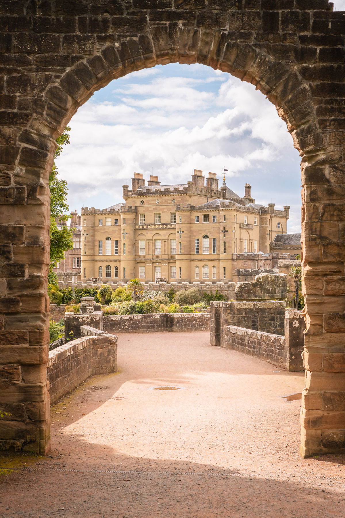 View of Culzean Castle in Ayrshire framed through a historic stone archway, with the castle's grand sandstone façade and surrounding grounds visible beyond