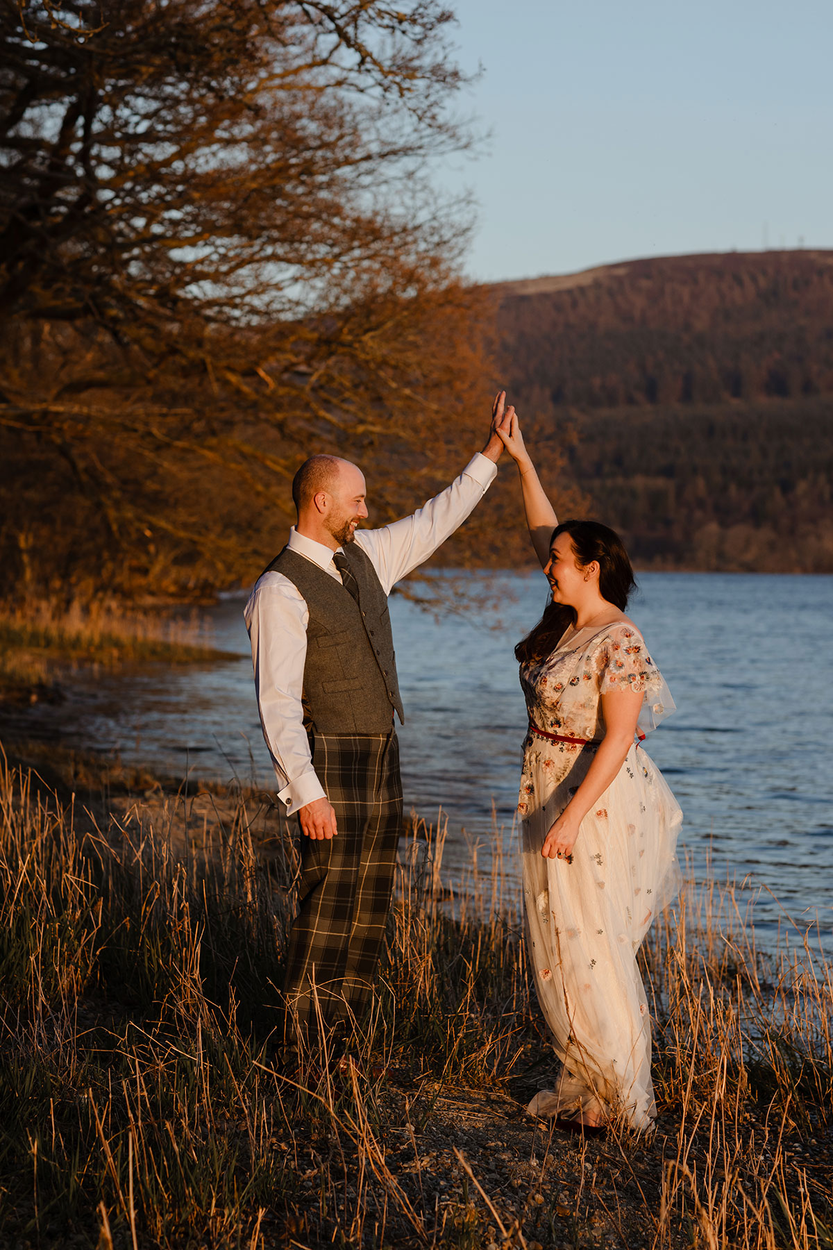 Bride and groom by the loch at sunset, holding hands 