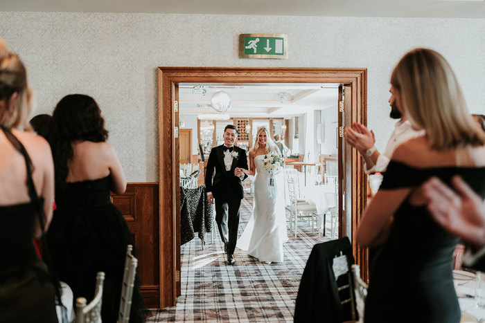 a bride and groom entering a room at busby hotel through a wooden door frame
