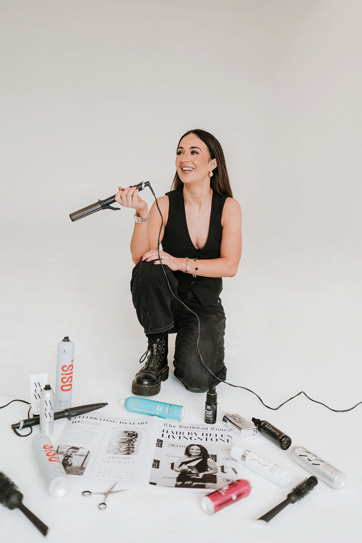 Bridal hairstylist Helen Livingstone holding a curling wand surrounded by professional hair styling products