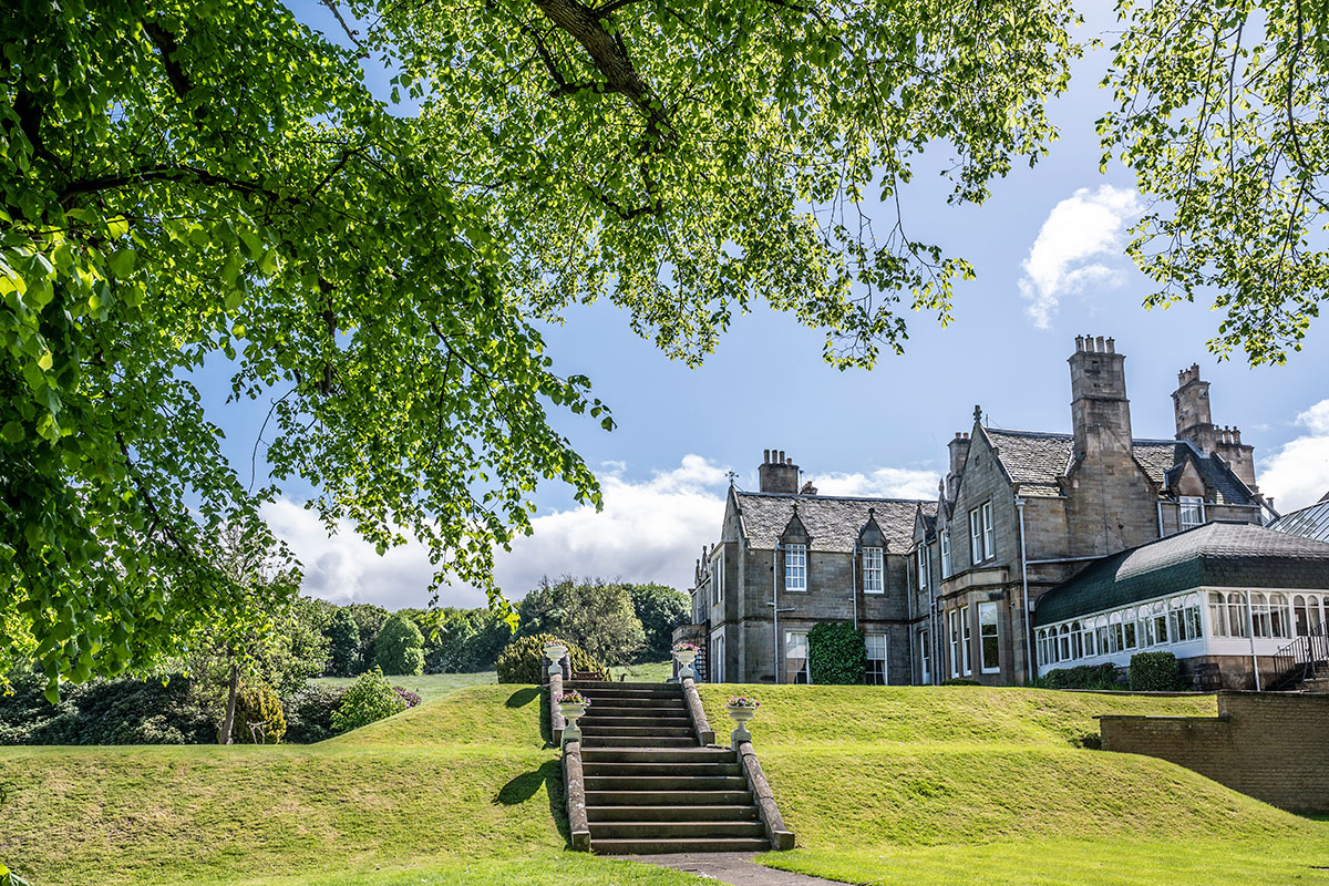 exterior of large grey home with conservatory attachment and a set of stone stairs leading down a grassy hill