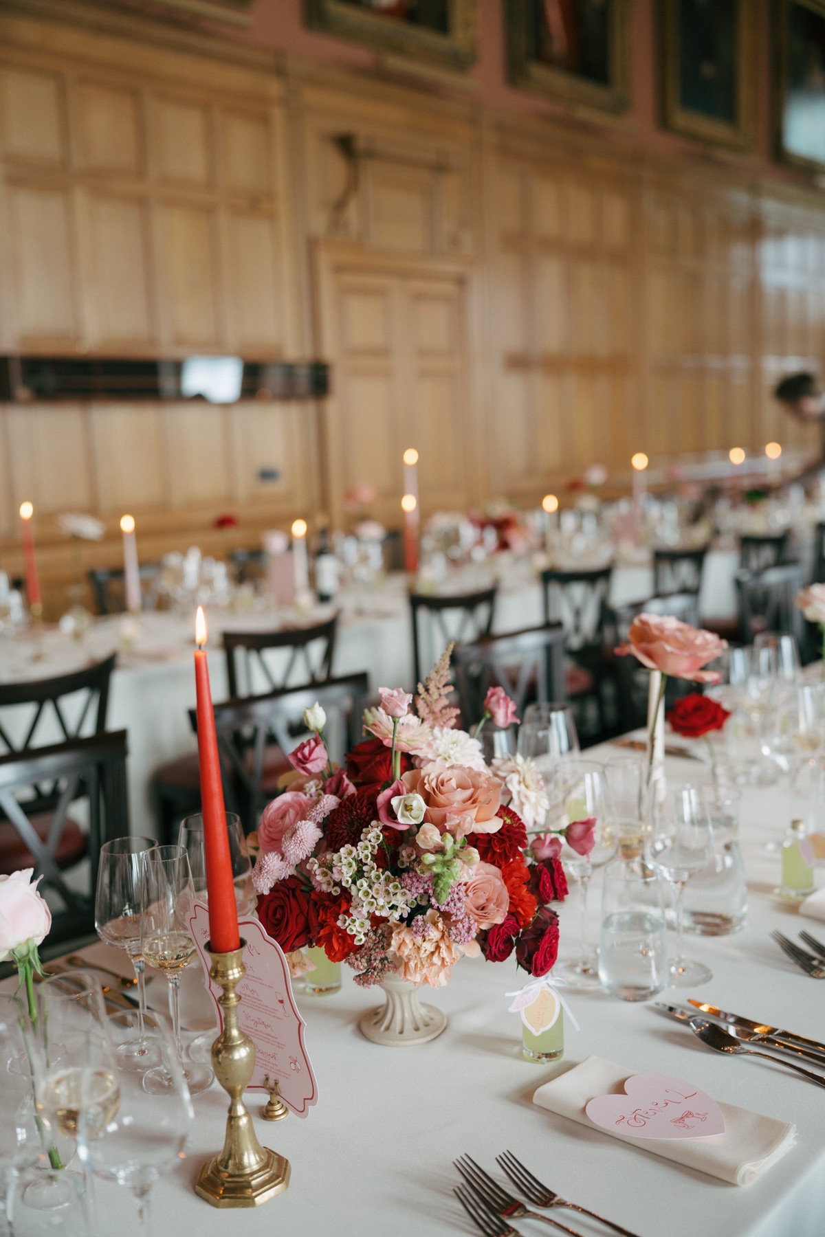 Wedding reception tables at Barnbougle Castle decorated by Gloam with vibrant pink-and-red flowers, taper candles and personalised stationery.