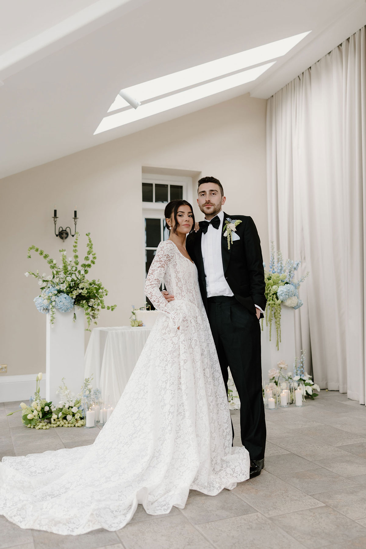 Bride and groom posing together in a bright reception space with floral displays and candles