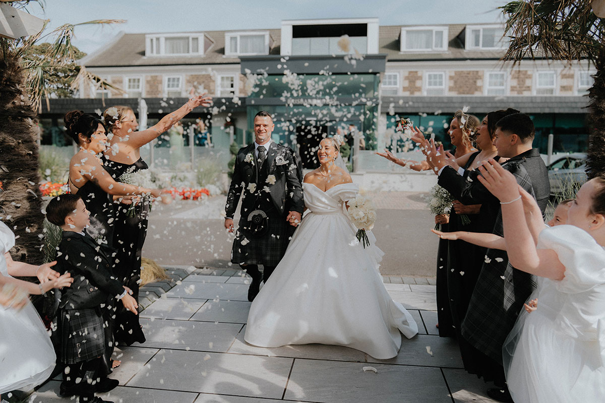 Newlywed couple walking through confetti outside Brisbane House Hotel in Largs after their Scottish hotel wedding ceremony.
