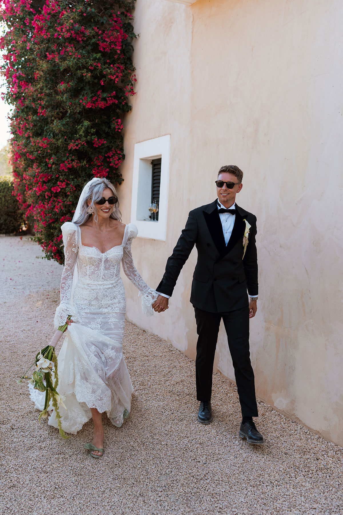 Bride and groom wearing sunglasses walking hand in hand outside Can Rafal Ibiza wedding villa after ceremony