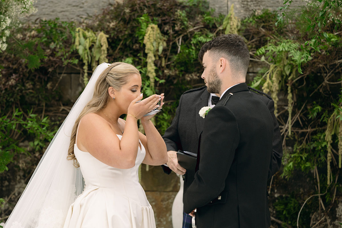 Bride and groom share whisky from a traditional Scottish quaich during their Dundas Castle outdoor wedding ceremony.