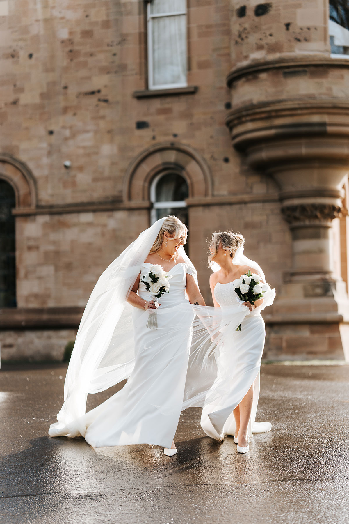 Newlywed brides walking hand in hand outside Cornhill Castle, their veils caught in the breeze in the golden afternoon light