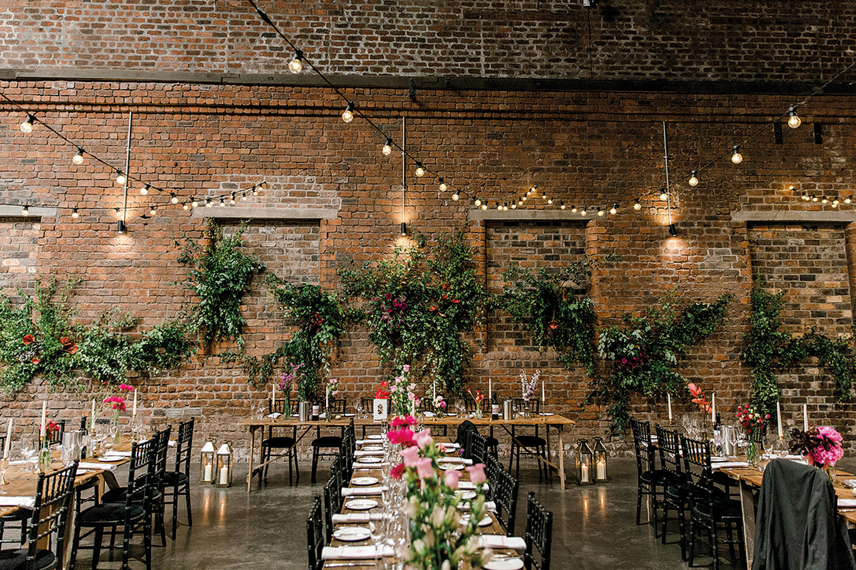 Industrial wedding reception setup with long tables, greenery and exposed brick at The Engine Works Glasgow