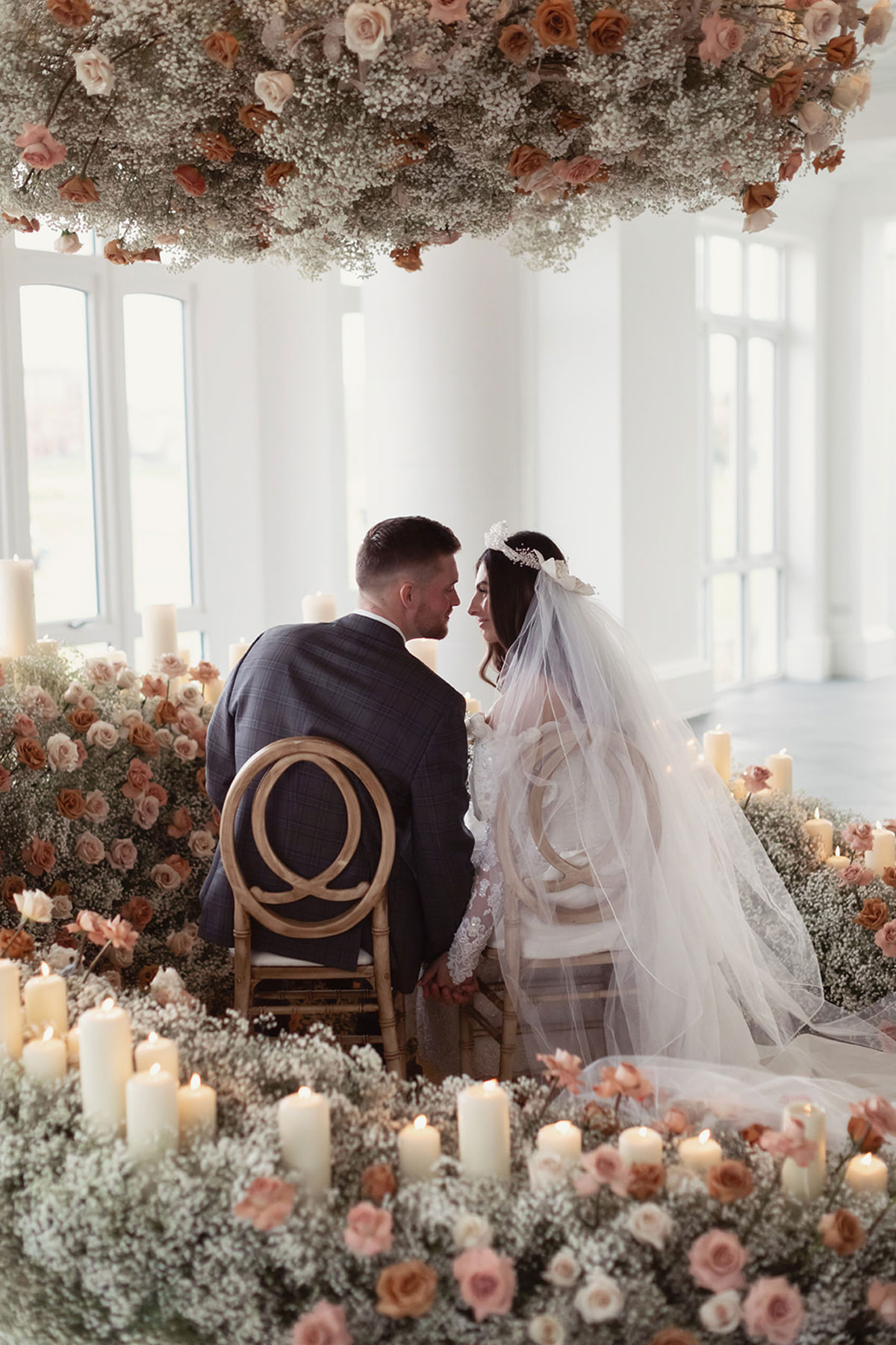 Bride and groom seated together in Old Course Hotel Conservatory surrounded by candles and floral ceremony styling, St Andrews