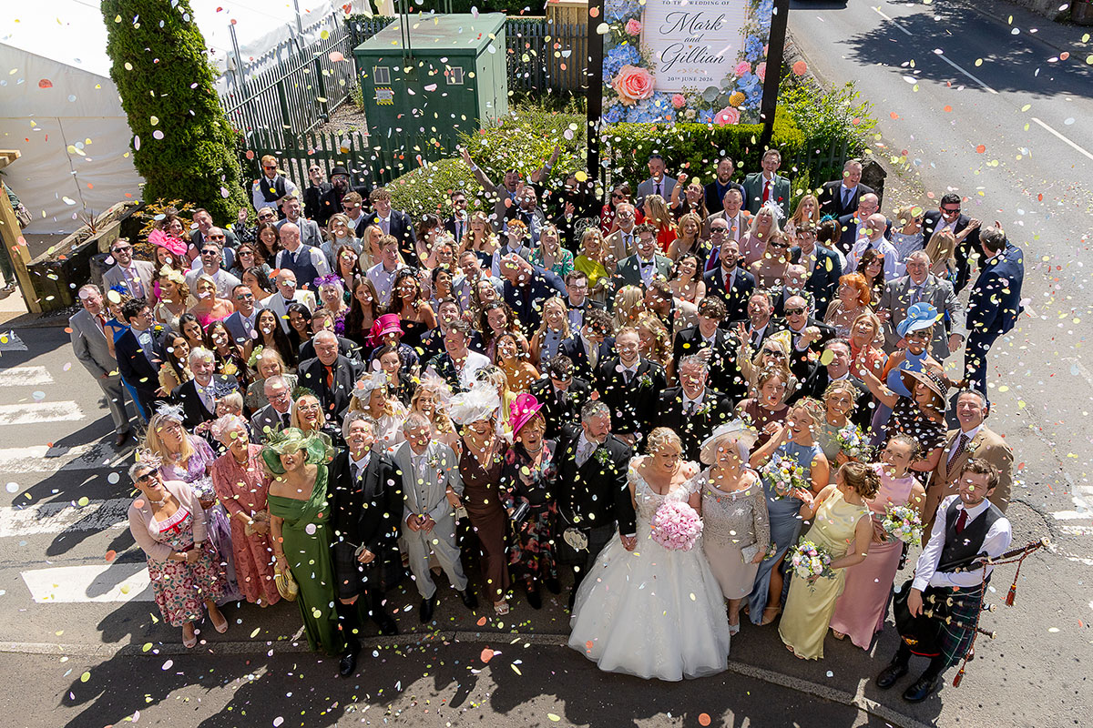 Large wedding group photo outside The River Inn in Renfrewshire with guests throwing colourful confetti.