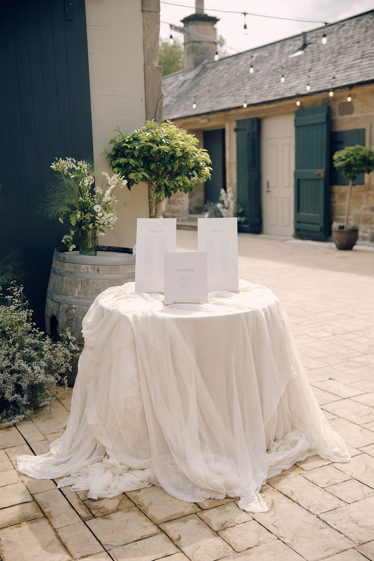 Wedding table plan displayed on draped round table in courtyard at Gilmerton House