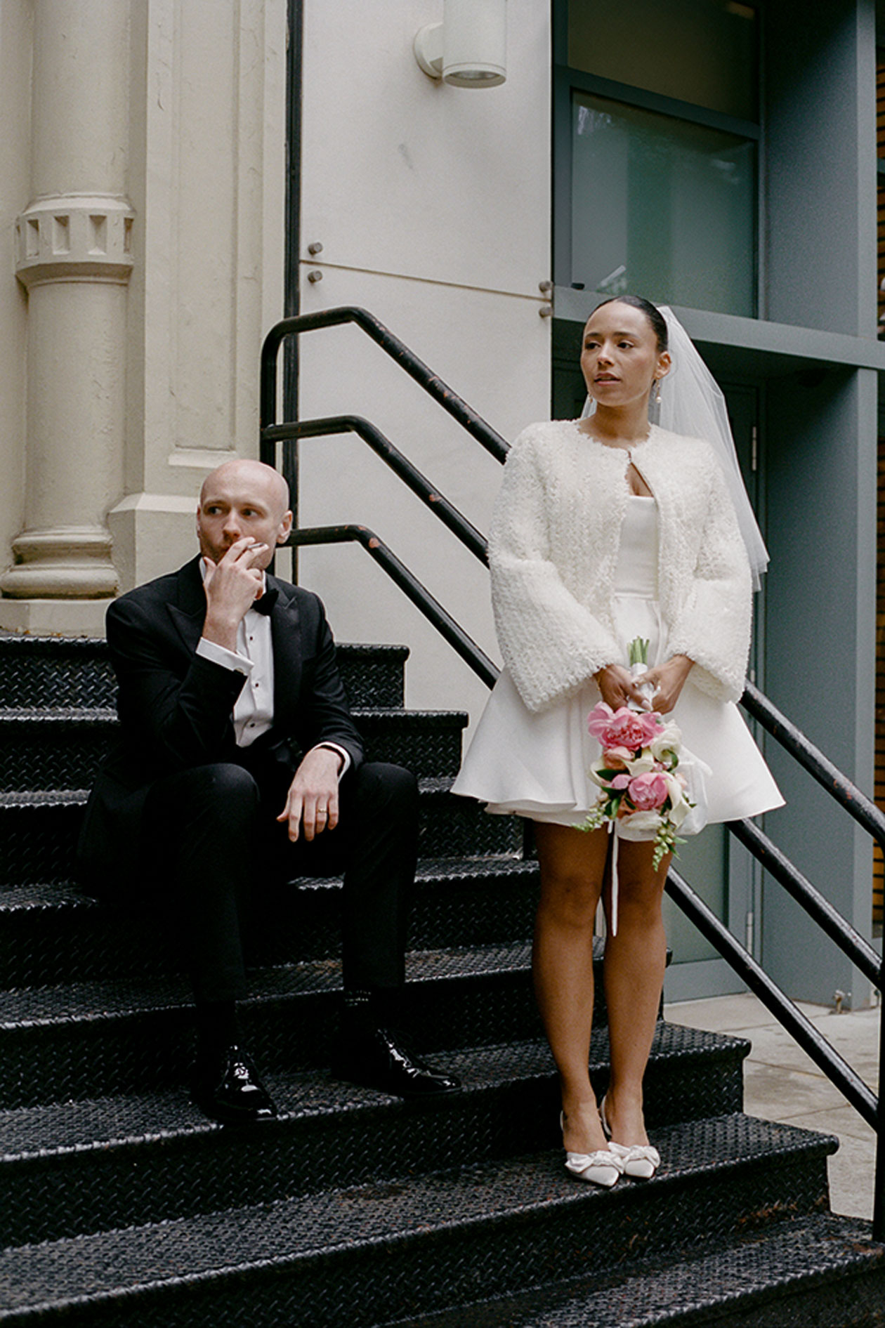 Bride and groom portrait on New York steps bride wearing short wedding dress and textured jacket holding bouquet