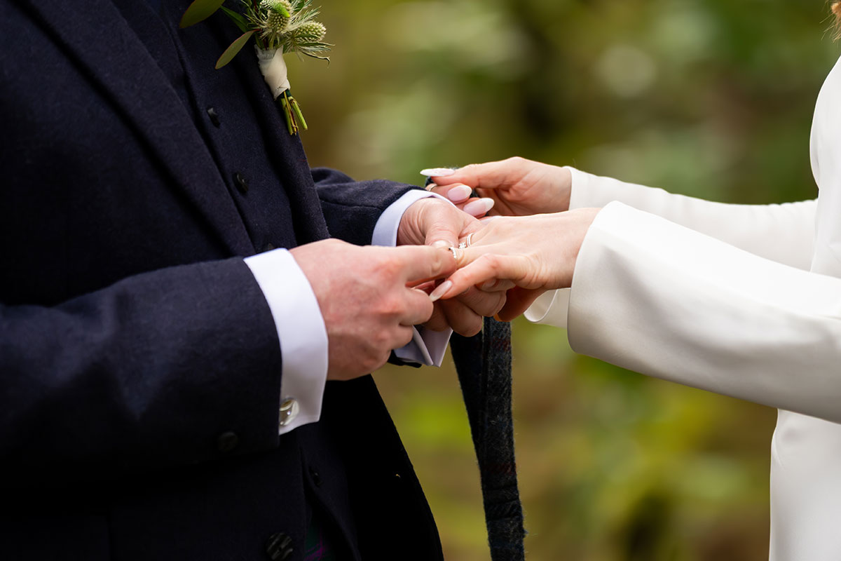 Close-up of the bride placing a wedding ring on the groom's finger during their outdoor Glencoe elopement ceremony