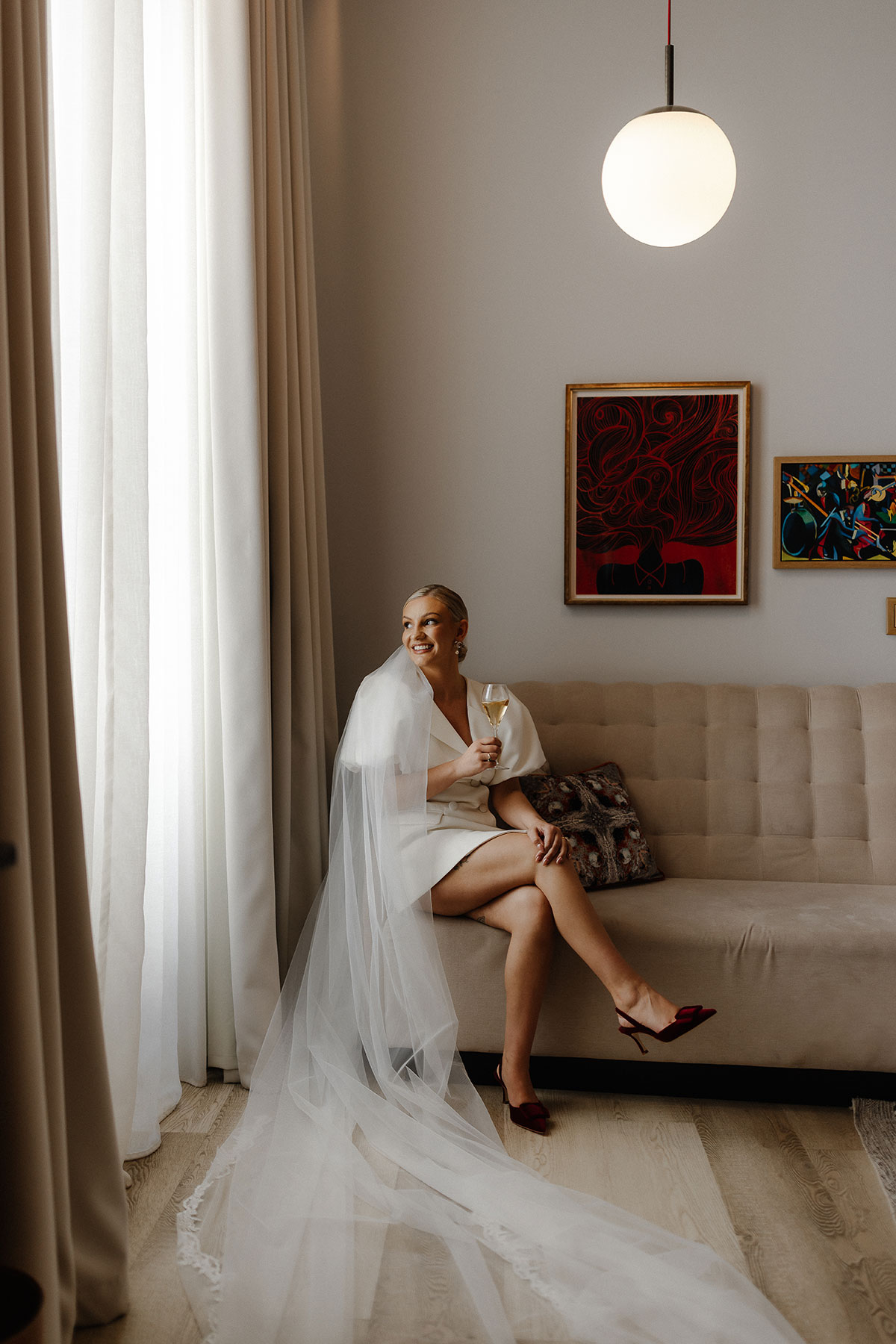 Bride in a short white blazer-style dress with a long veil, sitting on a sofa at Virgin Hotels Edinburgh before her registry office wedding, captured by Steph Nicol Photography.