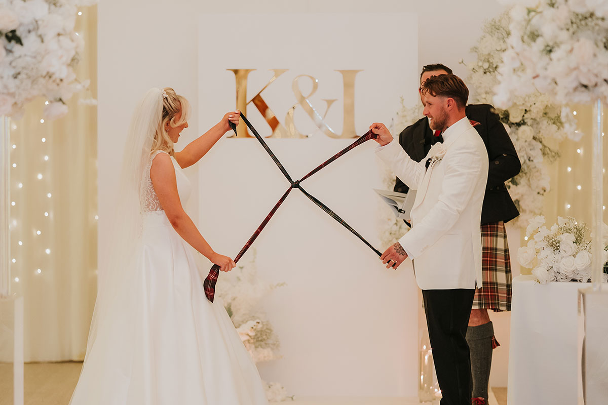Bride and groom taking part in handfasting ceremony with tartan ribbons at Ingliston Country Club wedding