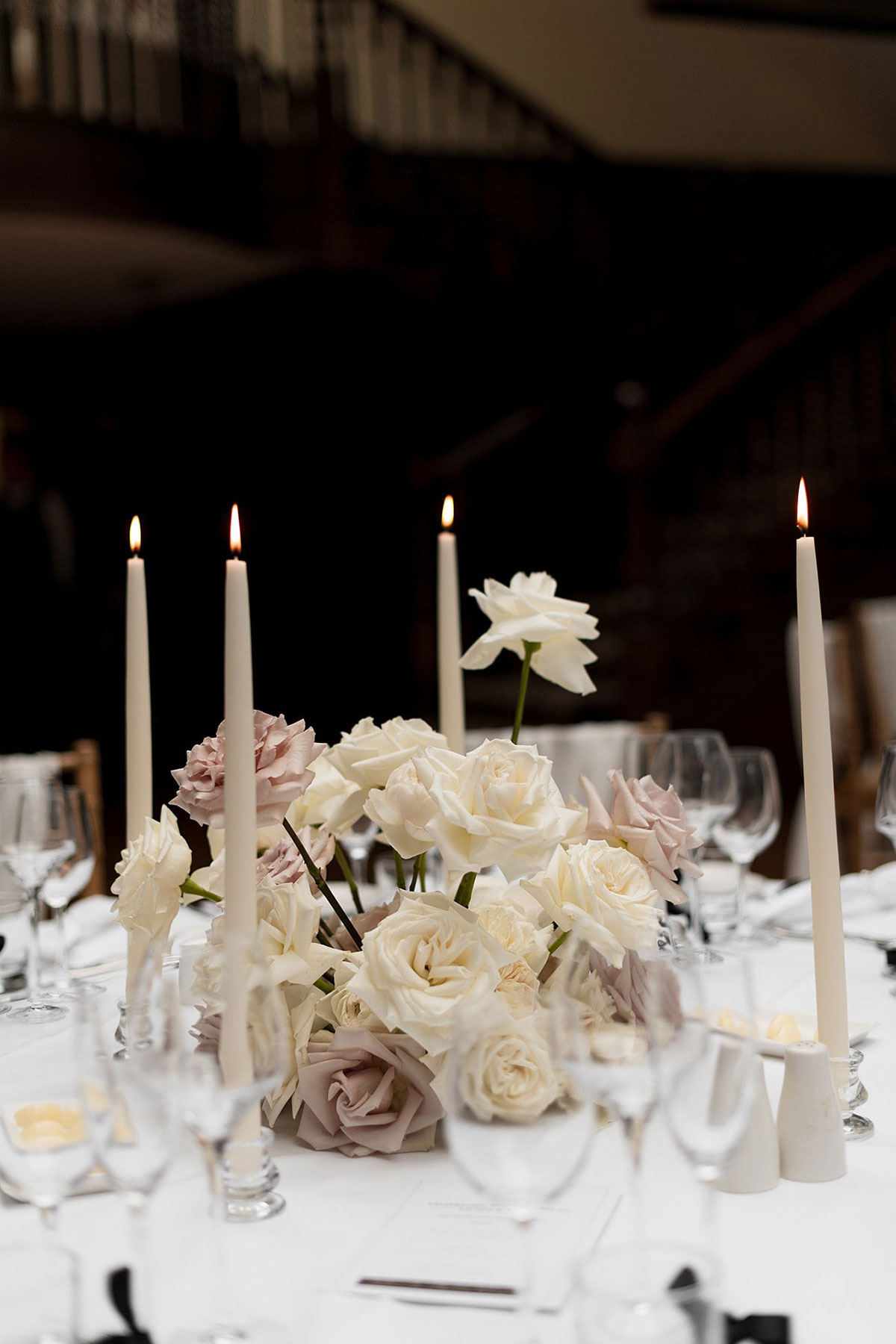 White and blush rose wedding centrepiece with tall tapered candles on a reception table at Crossbasket Castle in South Lanarkshire.