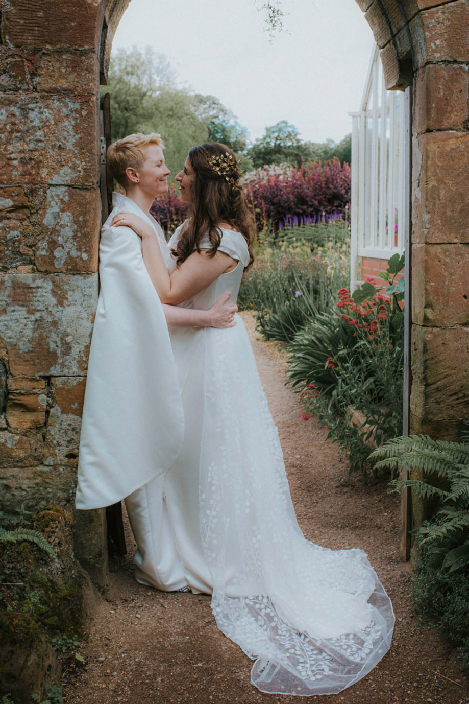 brides stand at entry way to cambo estate's walled garden and smile at one another