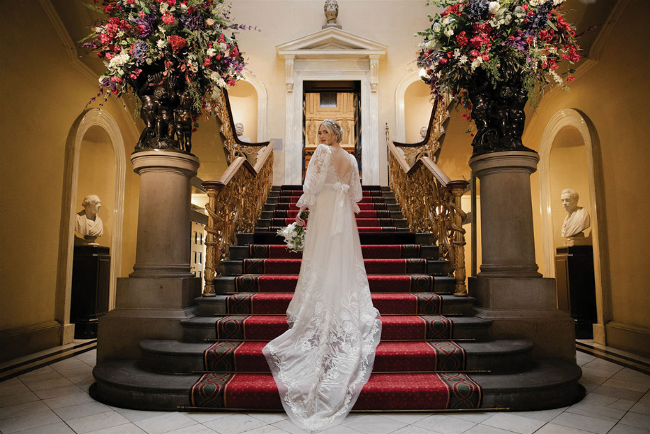 Bride on staircase looking back over her shoulder holding her bouquet