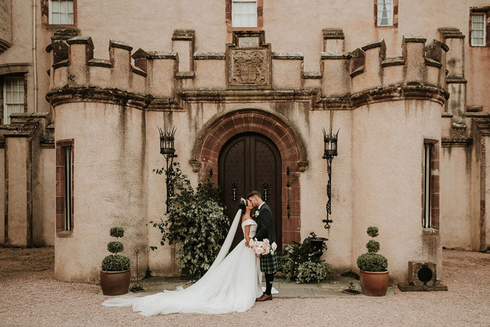 A bride and groom kiss in front of the wooden doors of a castle