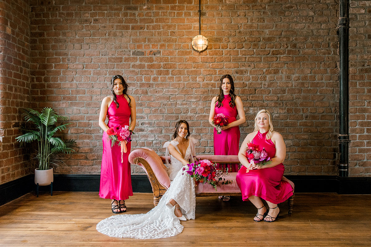Bride posing with three bridesmaids wearing bright pink satin dresses