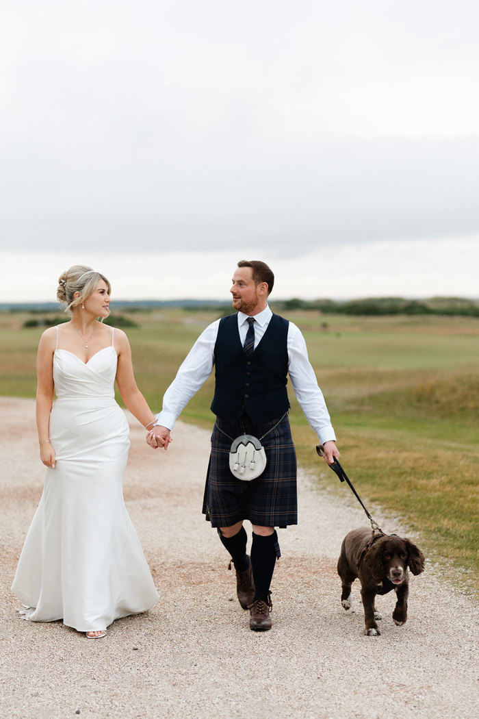 a bride and groom walking with a dog in the grounds of the Old Course Hotel.