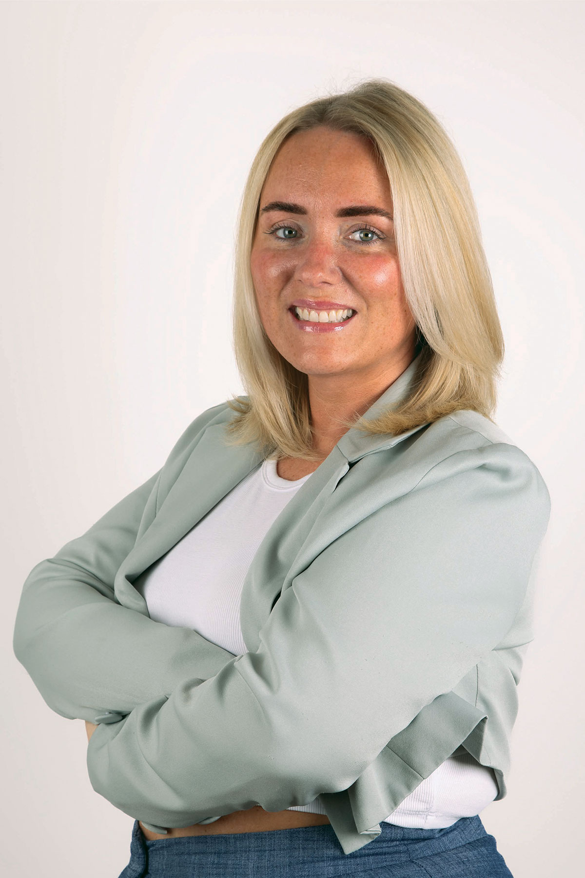 blonde woman with bob in pale seagreen blazer stands smiling with her arms crossed across chest