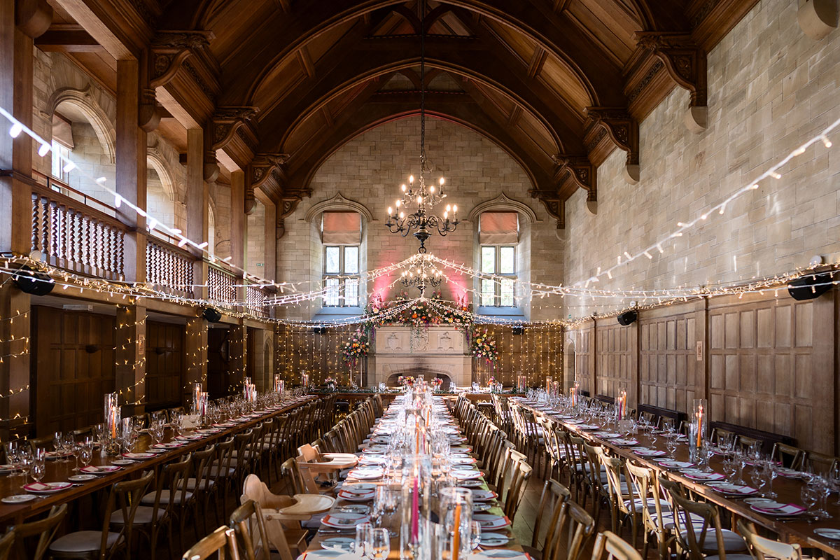 long wooden tables and matching chairs with white table cloths and colourful decorations set up for wedding dinner at achnagairn castle