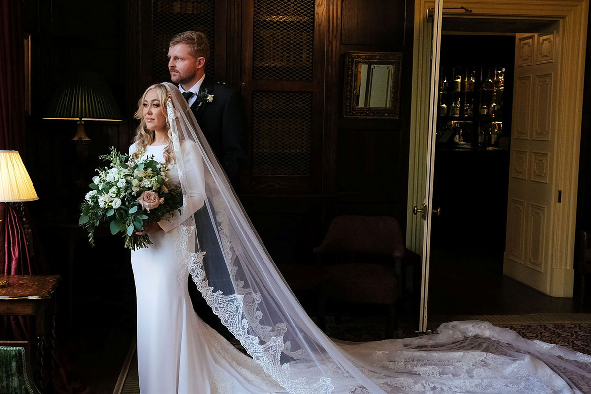 Bride and groom posing for a wedding portrait inside Crossbasket Castle with dark wood panelling and period interiors.