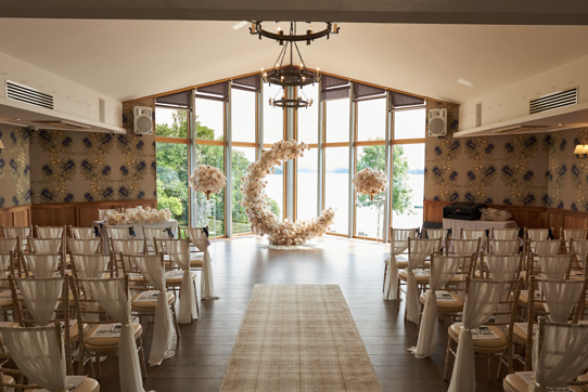 c shaped flower display at the top of aisle in front of large windows looking out to a body of water and greenery