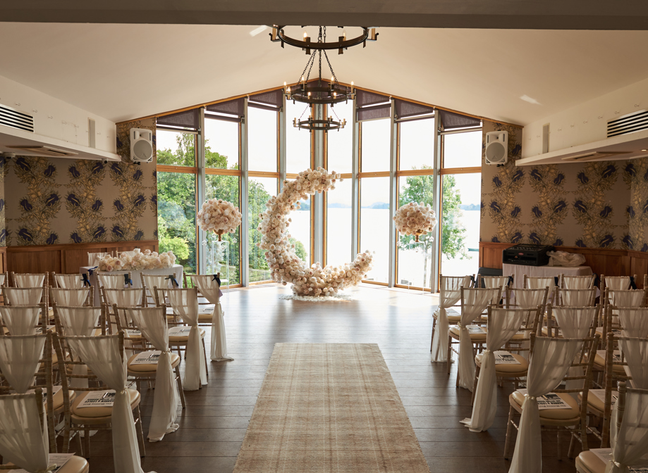 c shaped flower display at the top of aisle in front of large windows looking out to a body of water and greenery