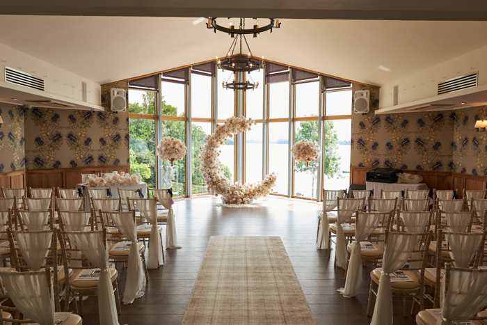 c shaped flower display at the top of aisle in front of large windows looking out to a body of water and greenery