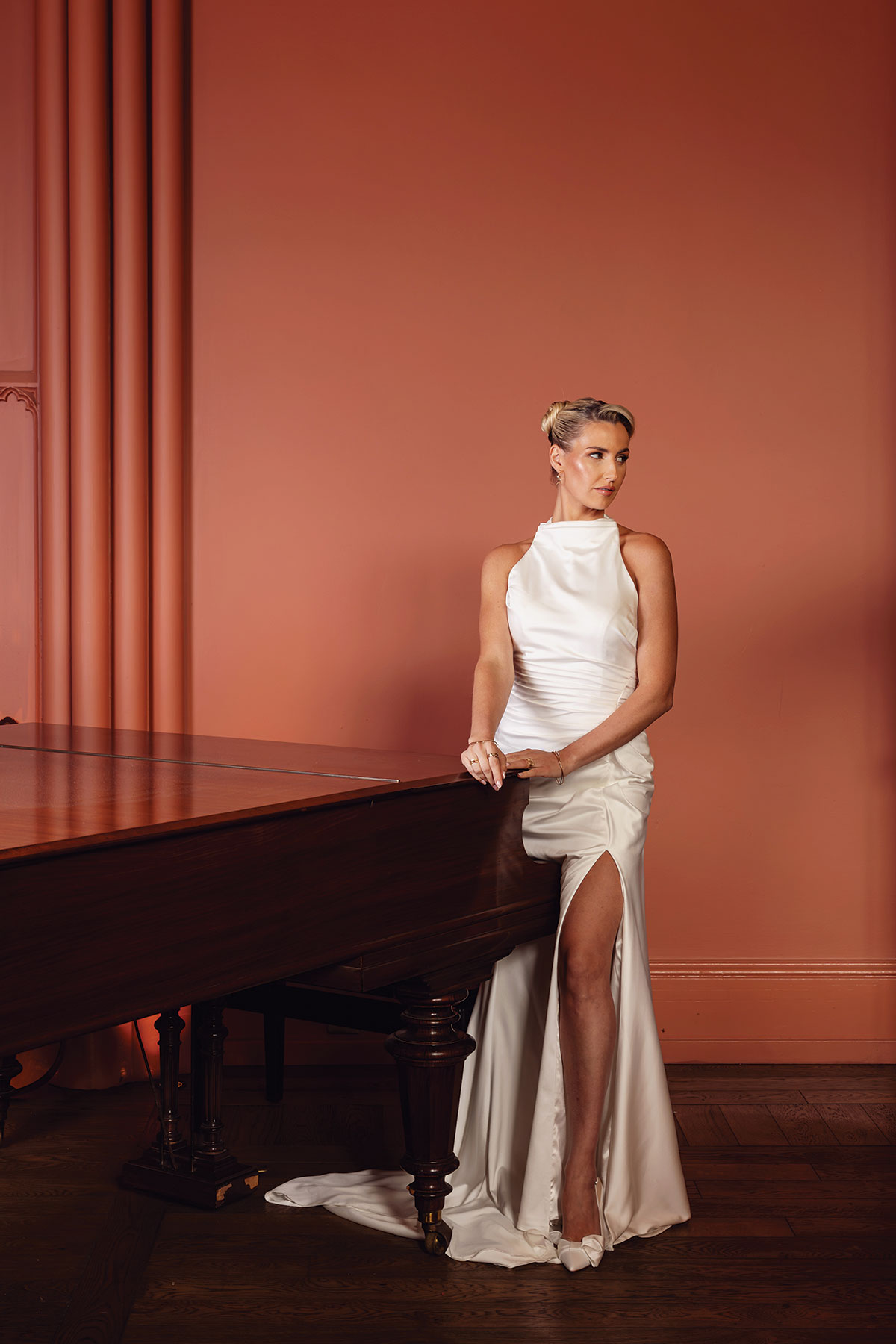Bride wearing elegant halterneck wedding dress and luxury bridal jewellery beside a grand piano at Mar Hall