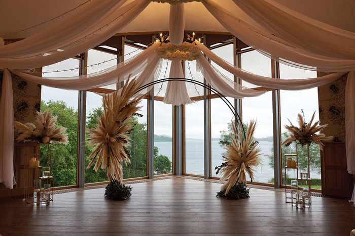 wedding ceremony set up at lodge on loch lomond with large windows and floral backdrop