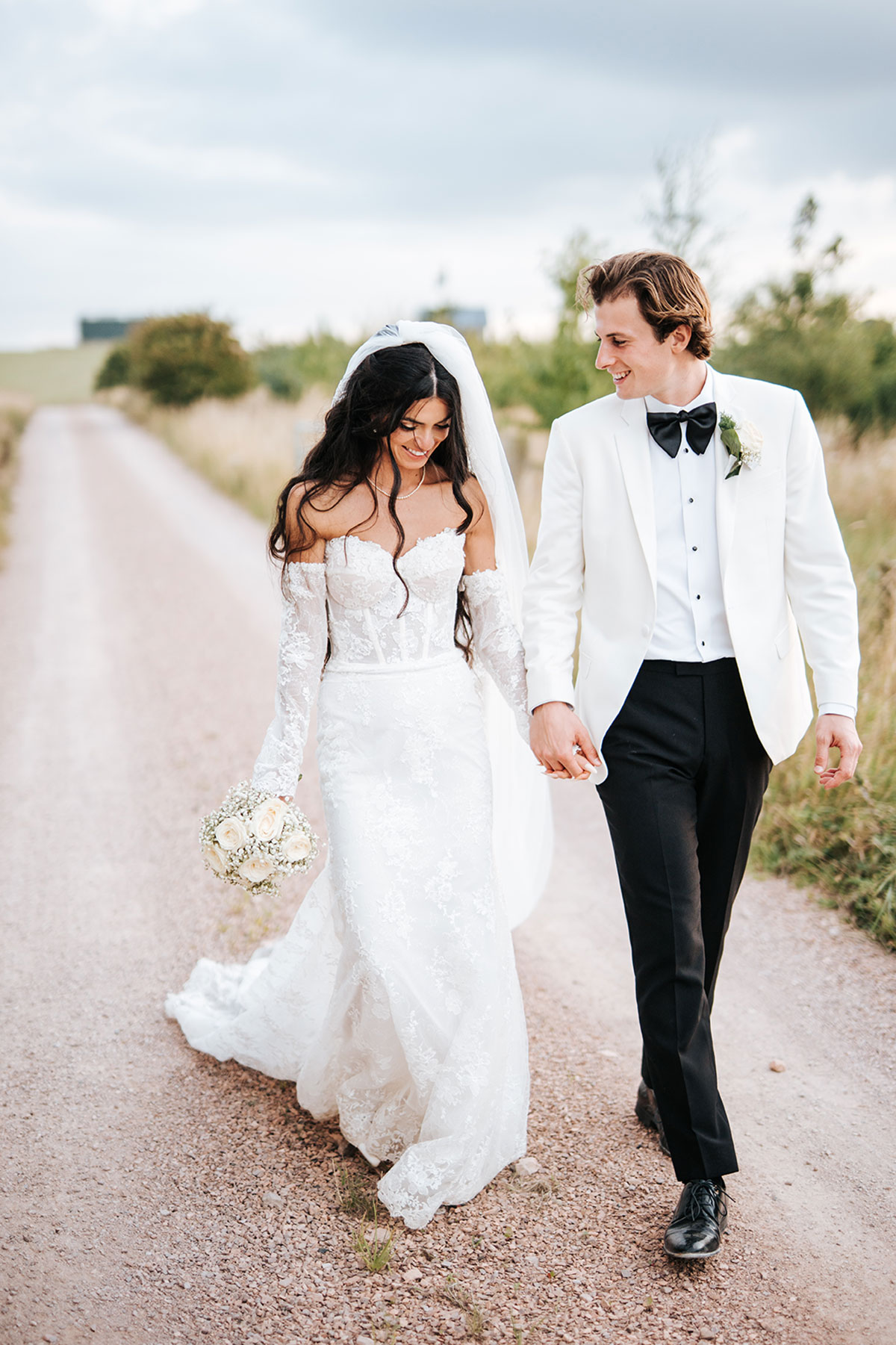 Bride and groom holding hands walking along a rural lane in wedding attire