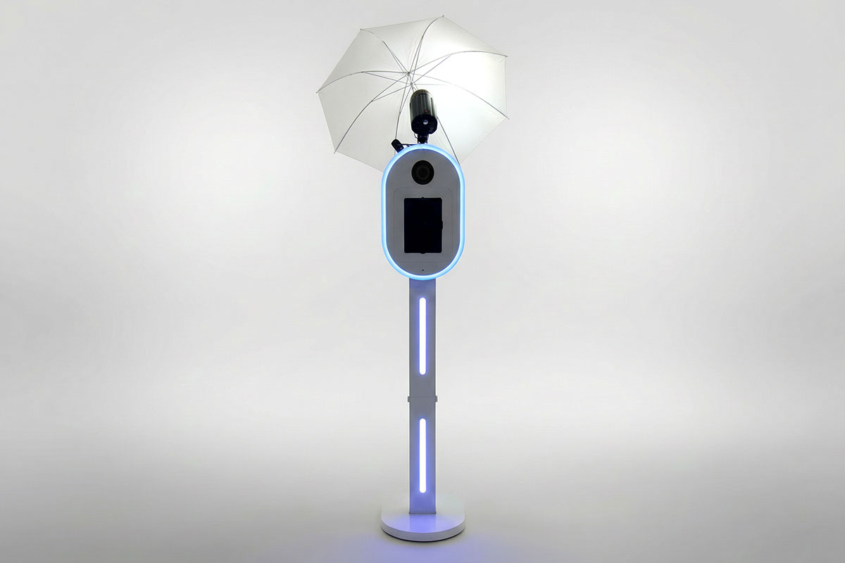 Full-length modern photo booth with LED lighting, studio umbrella flash and sleek white stand against plain backdrop