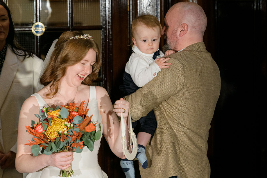 Bride holds autumnal bouquet in one hand and decorative horseshoe in the other