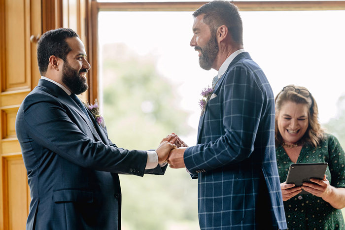 Grooms hold hands during wedding ceremony