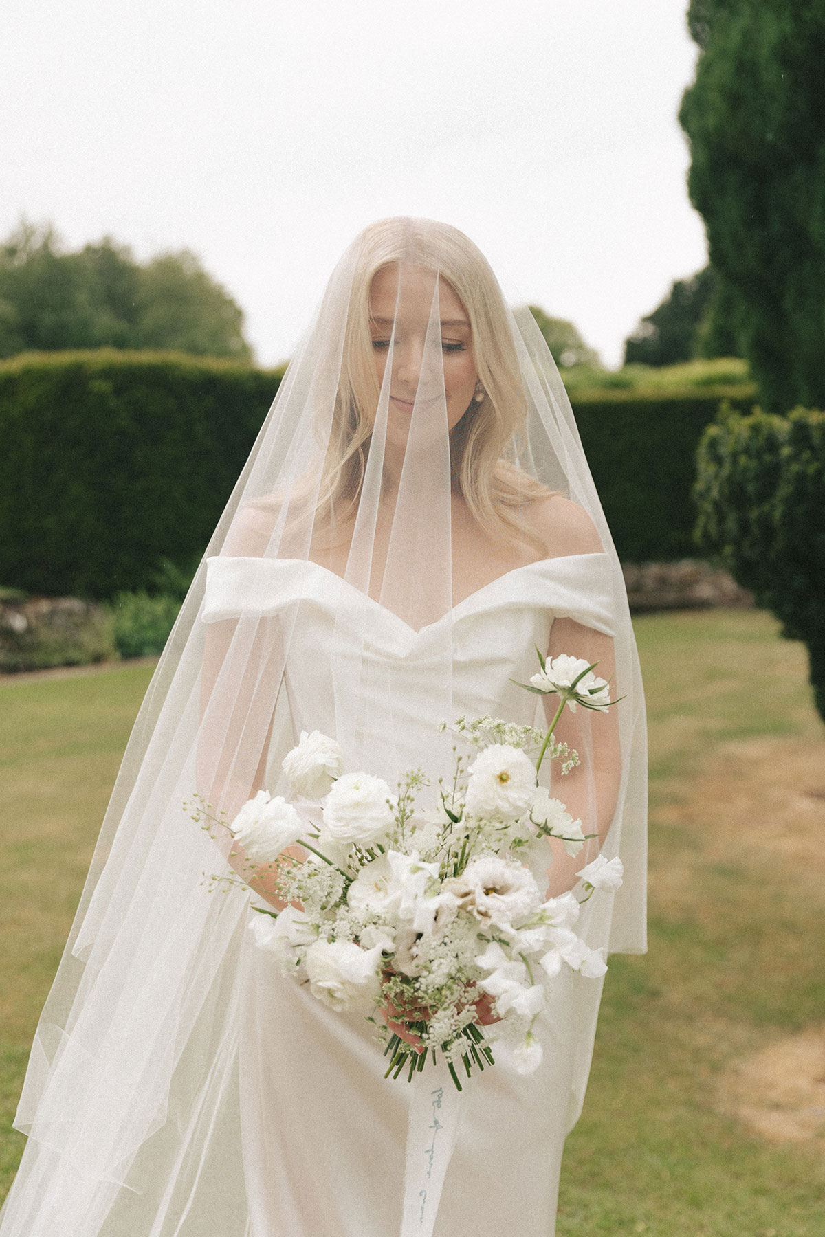 Bride wearing veil holding soft white bouquet in garden at Gilmerton House East Lothian wedding