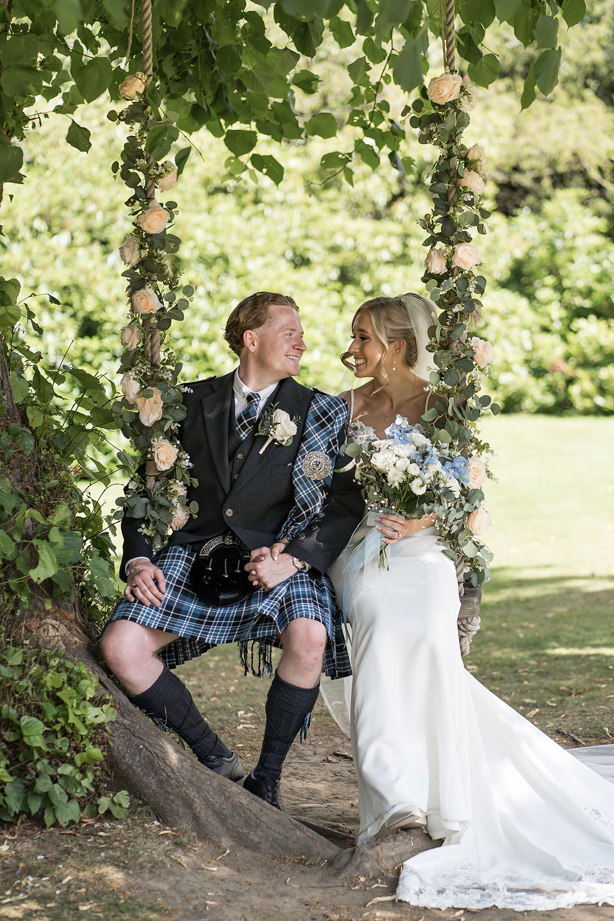 Bride and groom sitting on a floral swing in the grounds of Norton House Hotel & Spa near Edinburgh