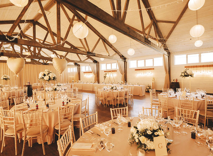 Wedding venue set up with round white tables, chairs and flowers with white paper lanterns hanging from the wooden rafters