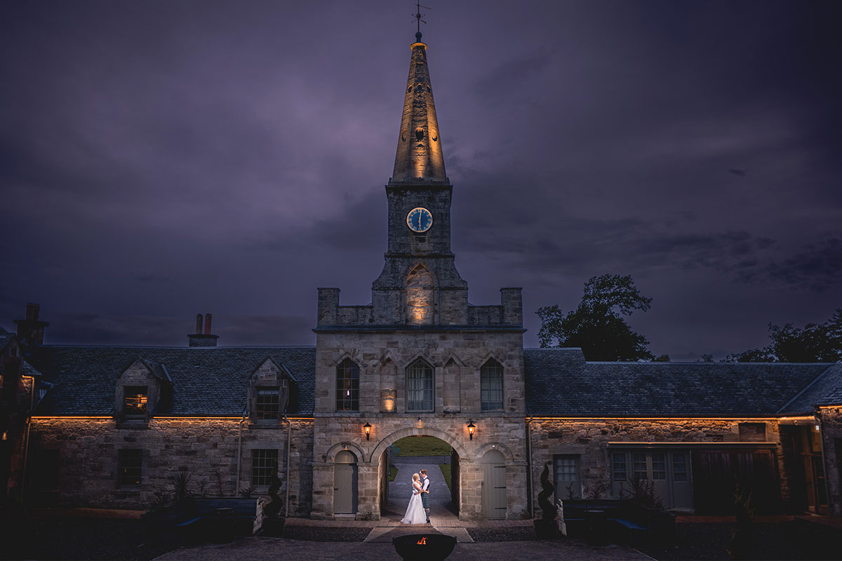 a couple standing in the archway of a stone building at night